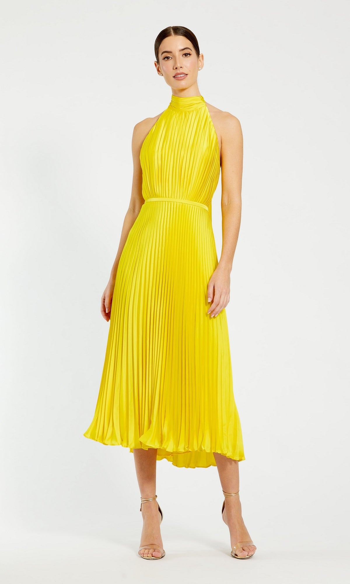 A woman stands against a white background wearing the Mac Duggal Tea Length Formal Dress 26909, a sleeveless yellow party dress with a high neck, pleated tea-length skirt, and strappy heels.